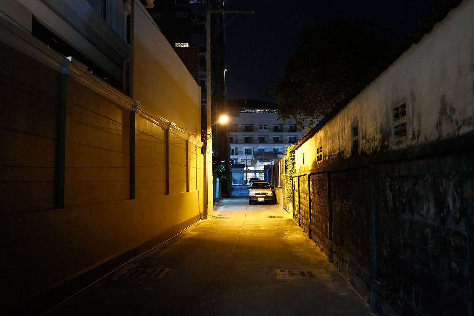 Carro solitário estacionado num beco escuro à noite, sob a luz de um candeeiro